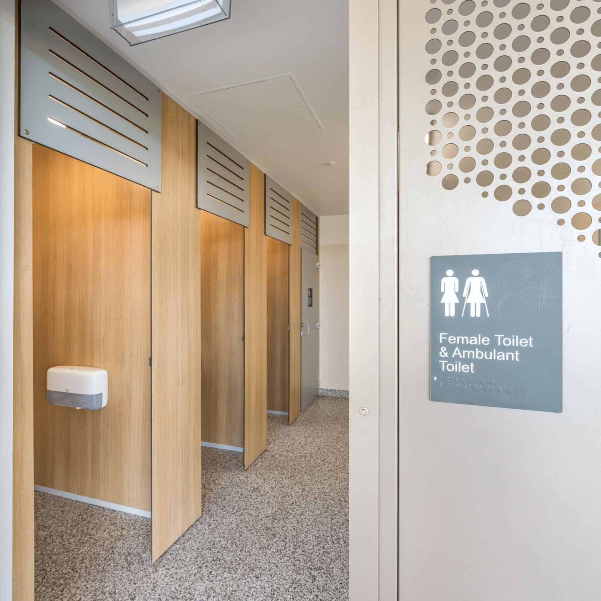 School amenity block with woodgrain and grey compact laminate cubicles and slatted bench seating