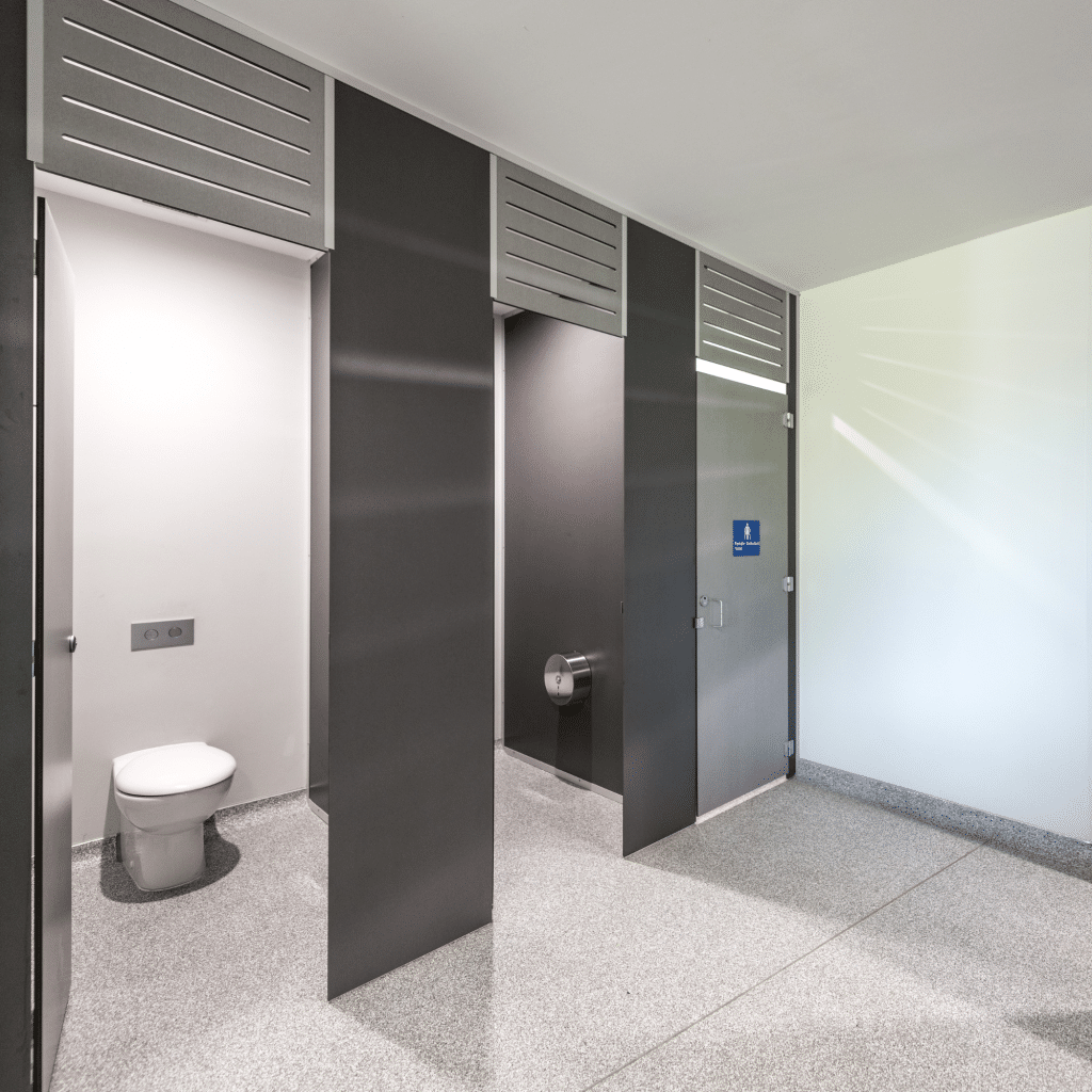 Dark grey full-height toilet partitions in a school washroom with terrazzo flooring
